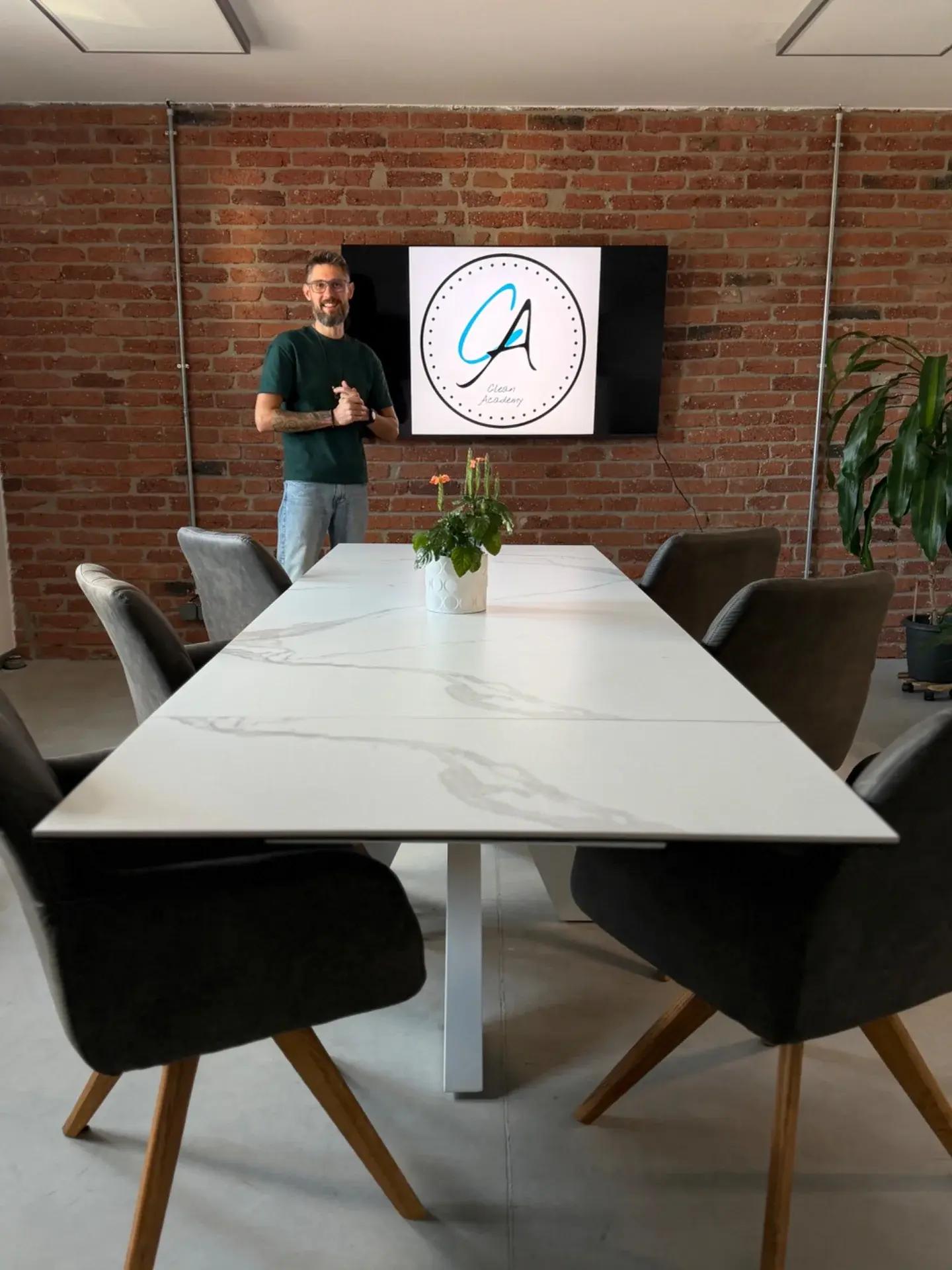 Petr Jileček u obrazovky s logem Clean Academy v místnosti se společným stolem